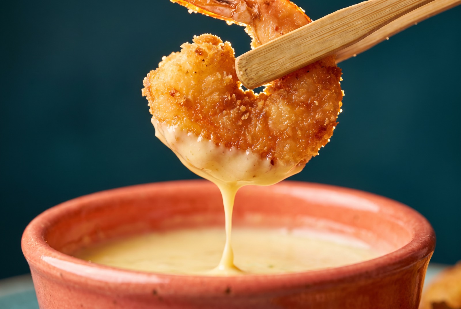 Fried shrimp lifted with bamboo tongs, sauce dripping
