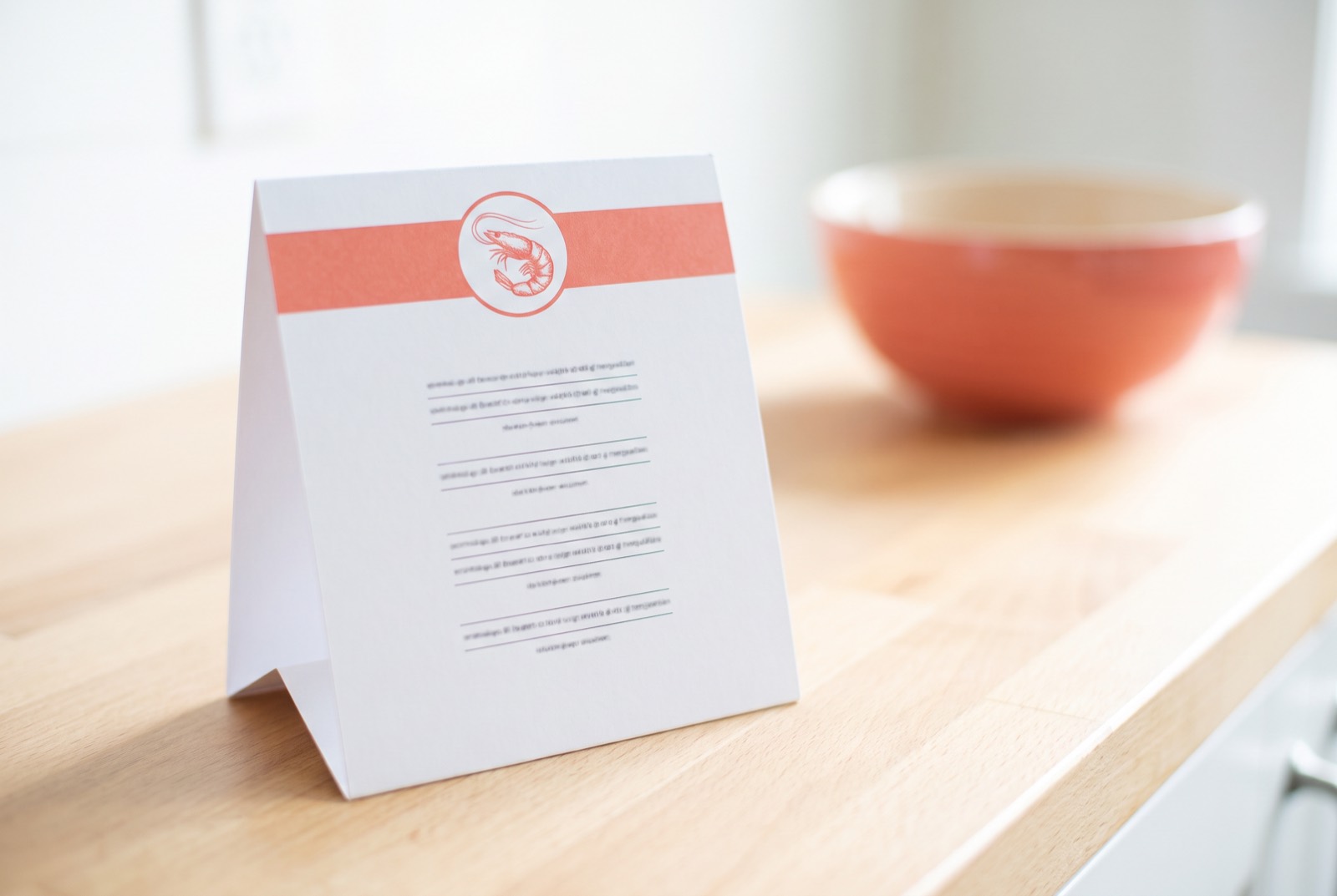 White table tent card with coral band and shrimp roundel on the counter