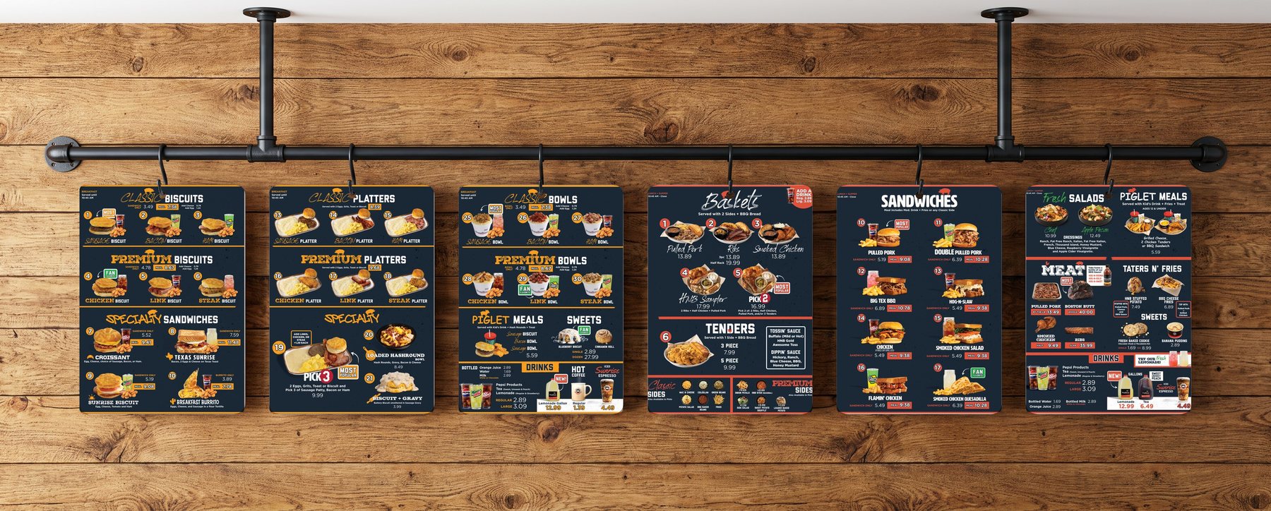 Six 18 by 24 inch polymetal menu panels hanging from S-hooks on a cast iron pipe rail on a wood wall — Hog-N-Bones breakfast and lunch menus