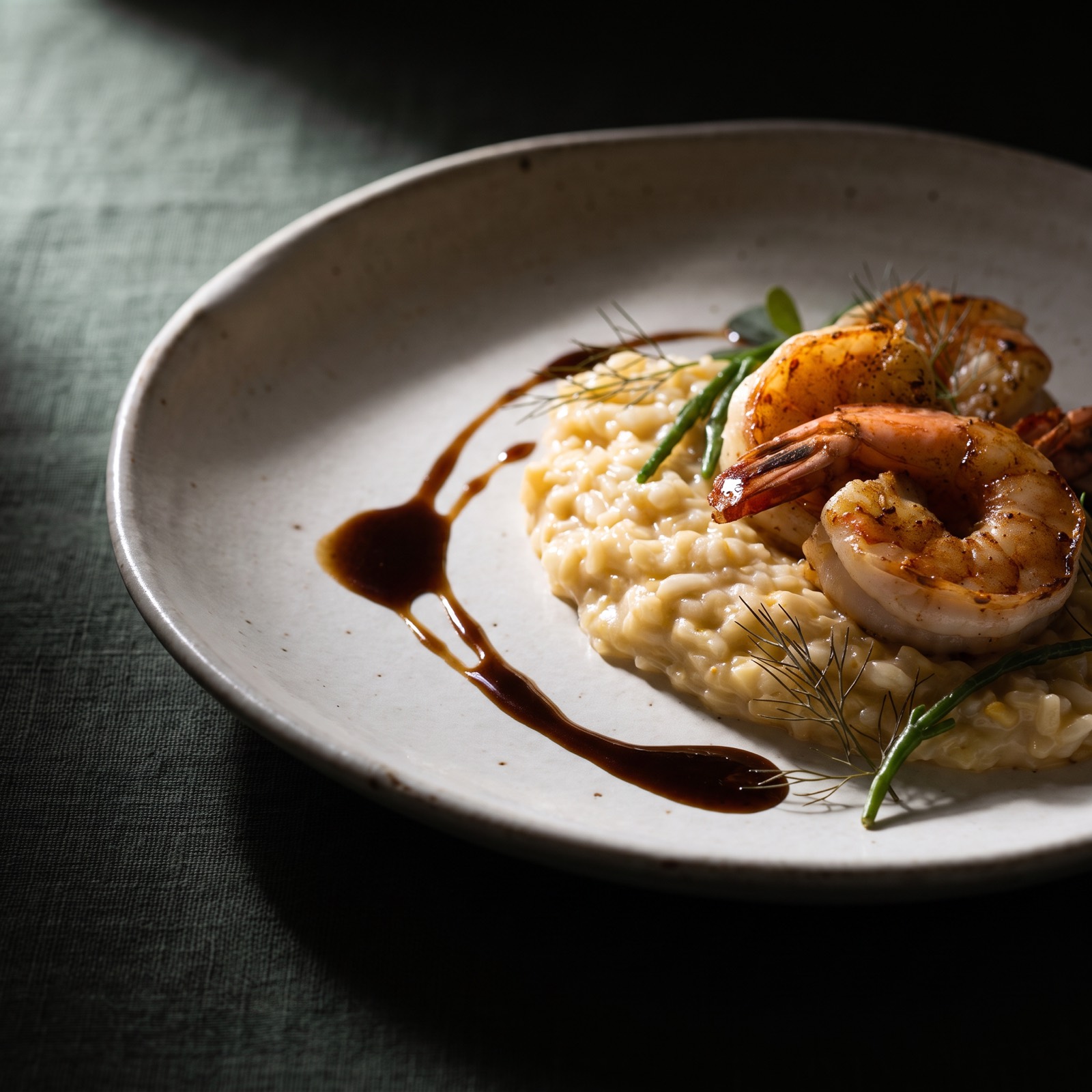 Cast-net shrimp over Carolina Gold rice cream with a shellfish glaze swoosh on stoneware, green linen beneath