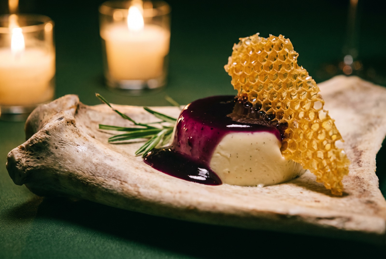 Sweetgrass panna cotta with muscadine and a honeycomb shard on driftwood, candlelit