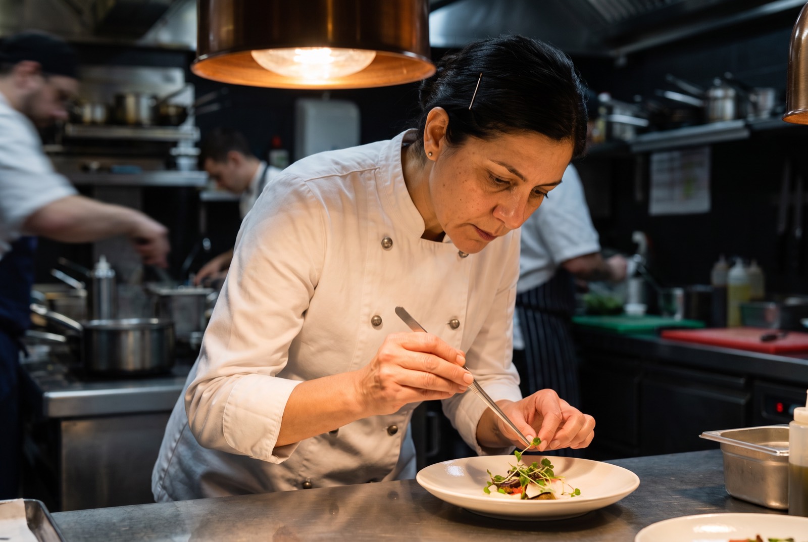 The chef leaning over the pass, placing the final garnish with tweezers