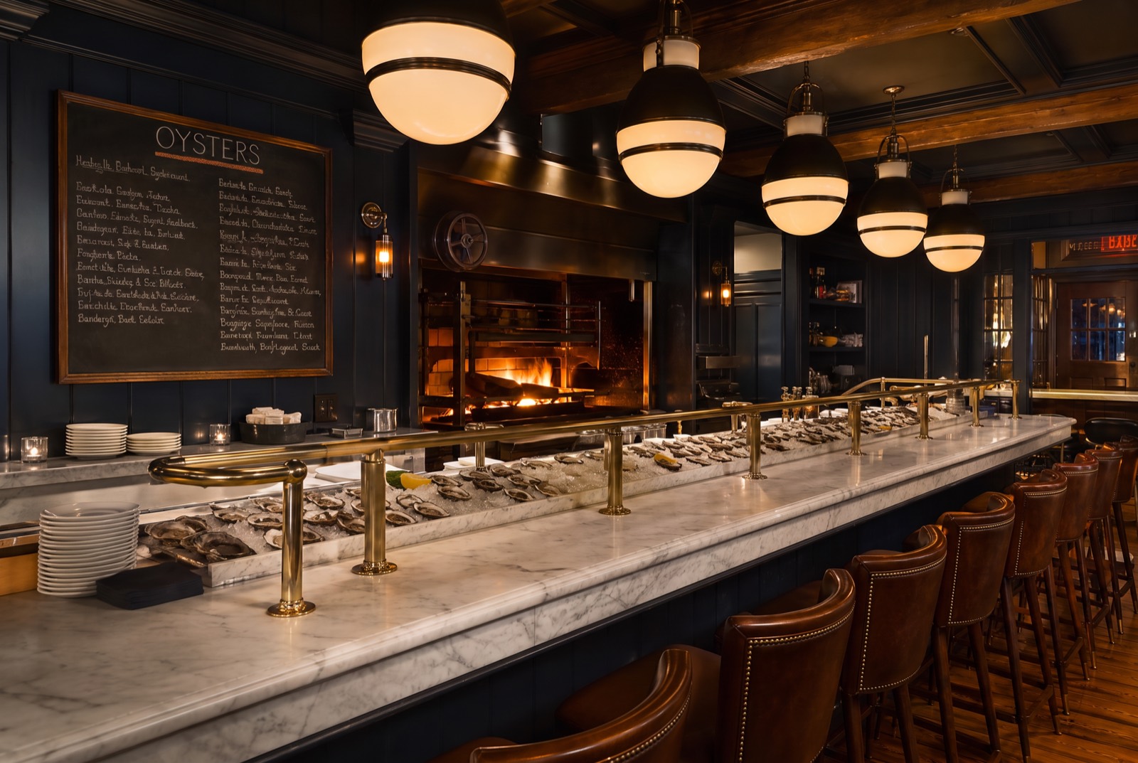 The oyster hall with marble raw bar, brass rails, wood fire, and the chalkboard oyster list